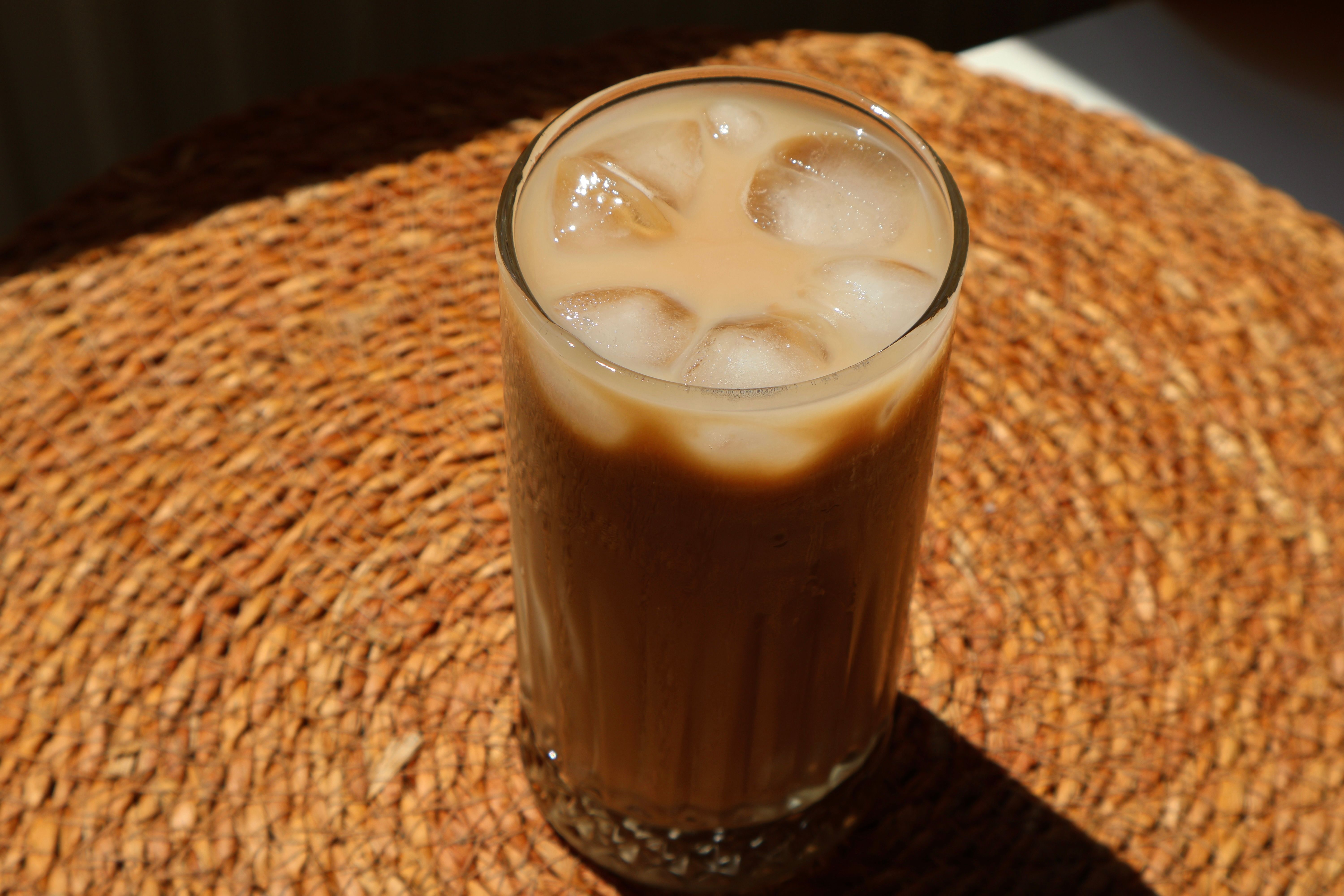 Tall glass of iced latte with milk swirling in coffee