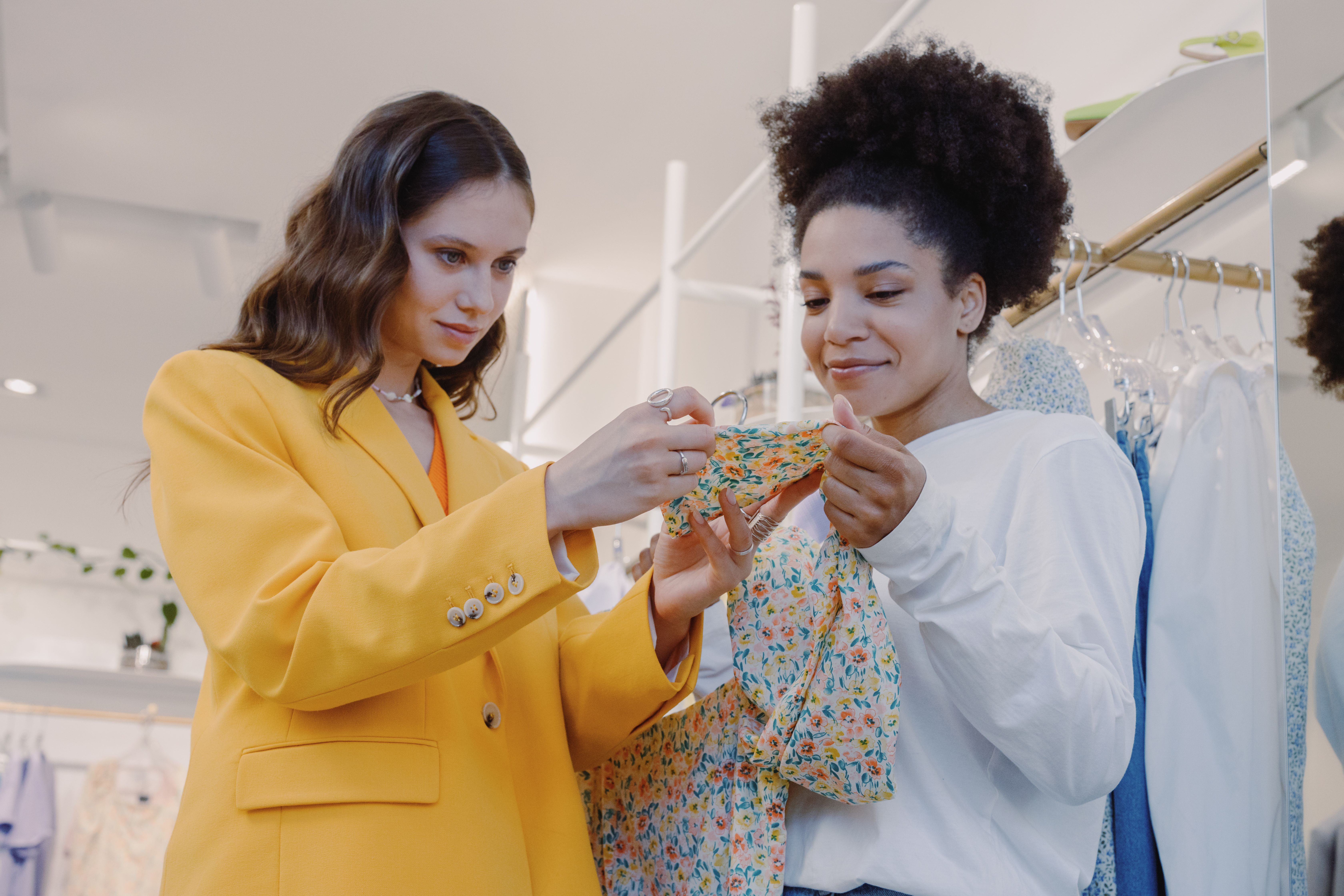 Two women smiling while arranging a vintage clothing display in a cozy shop