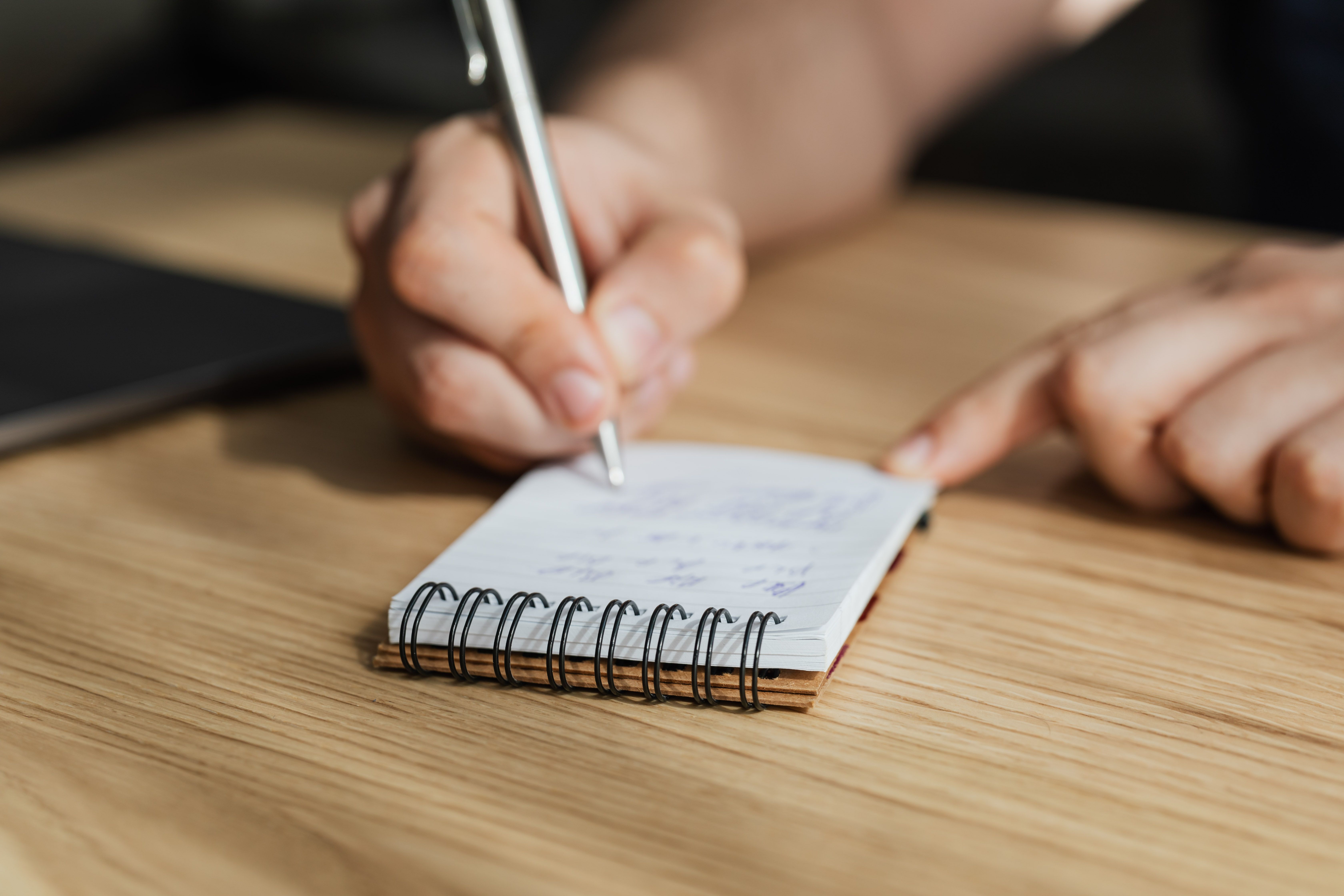 Person writing in a notebook with a silver pen