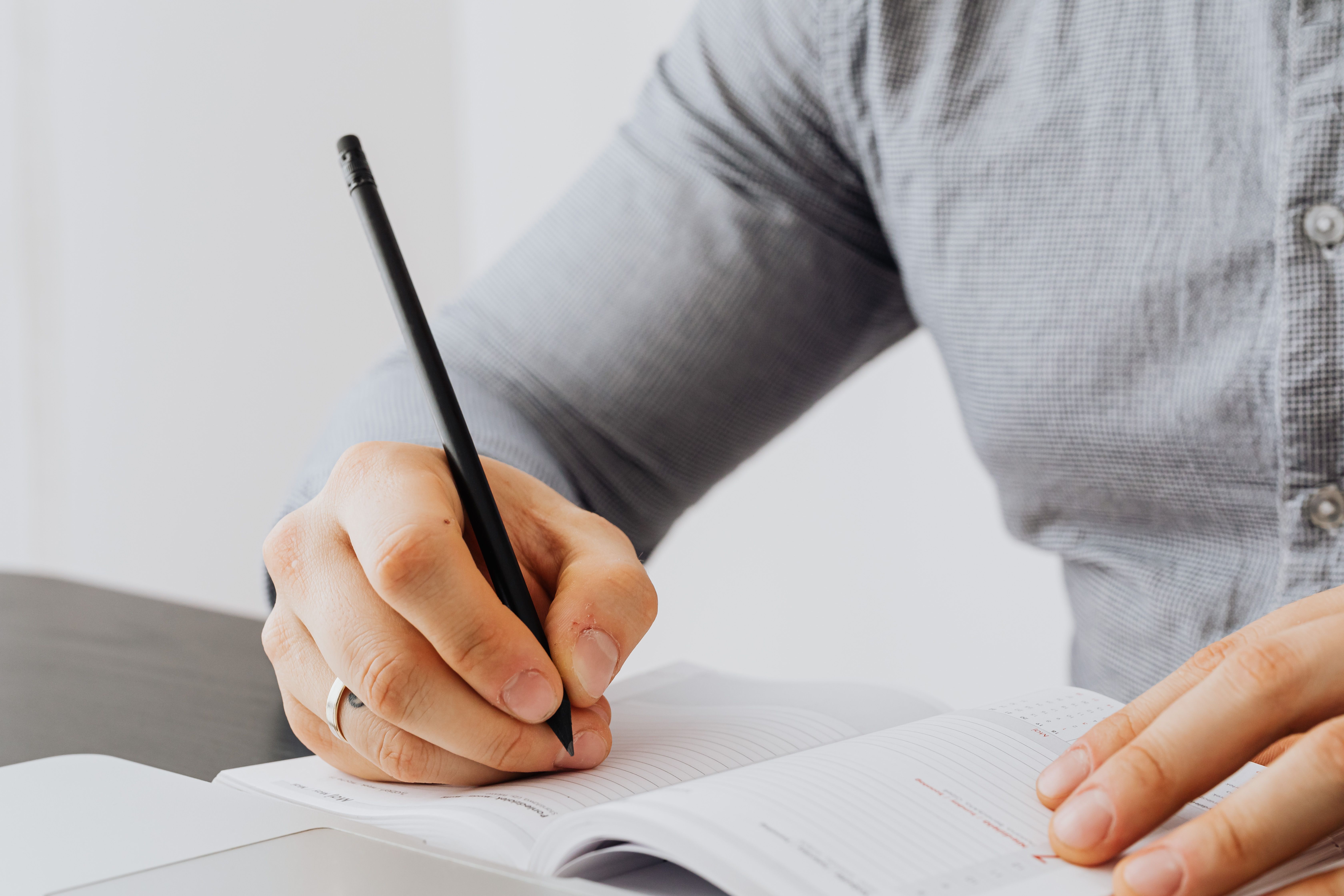 Close-up of hands writing in a notebook next to a laptop