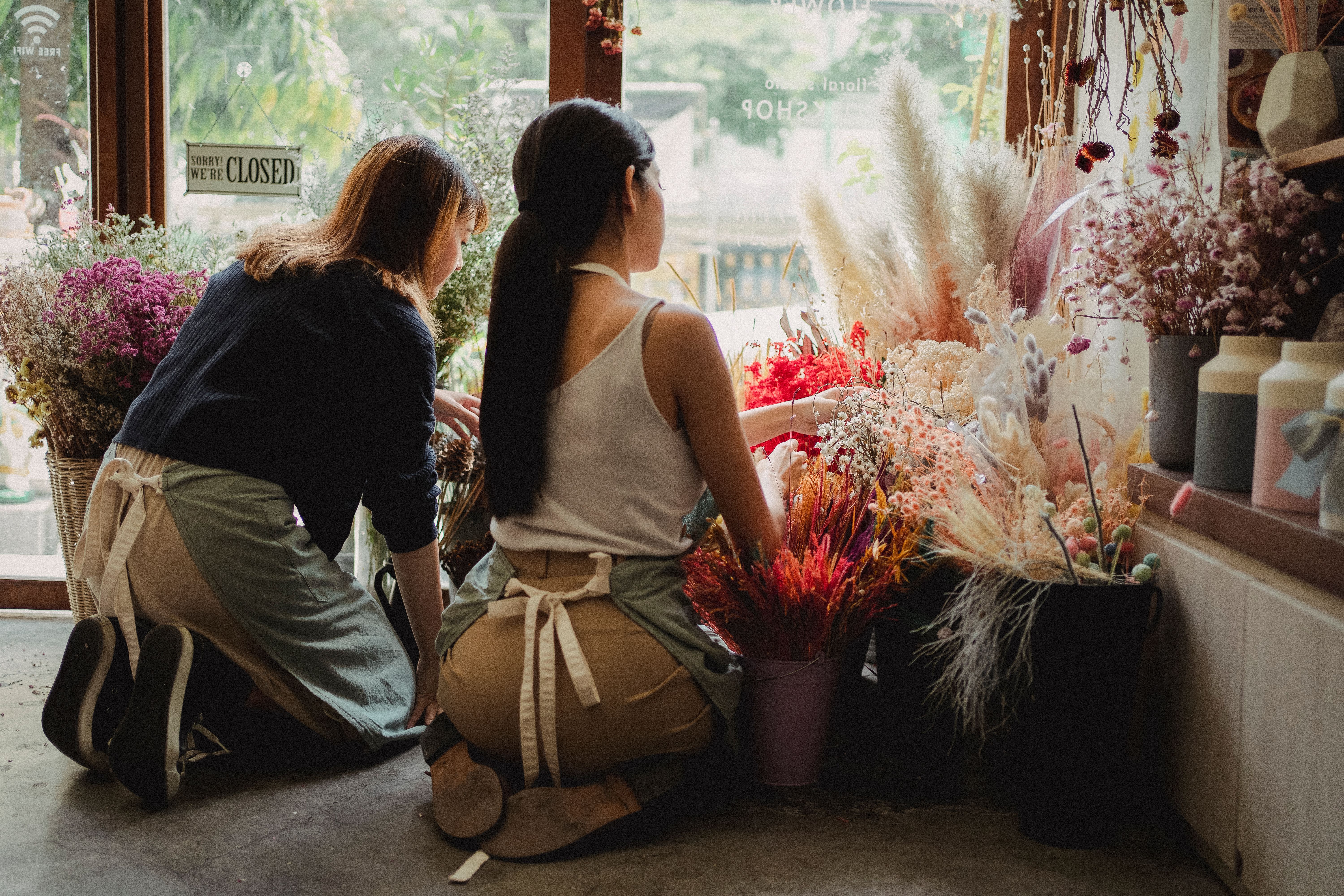 Two women organizing a clothing display in a sunlit shop