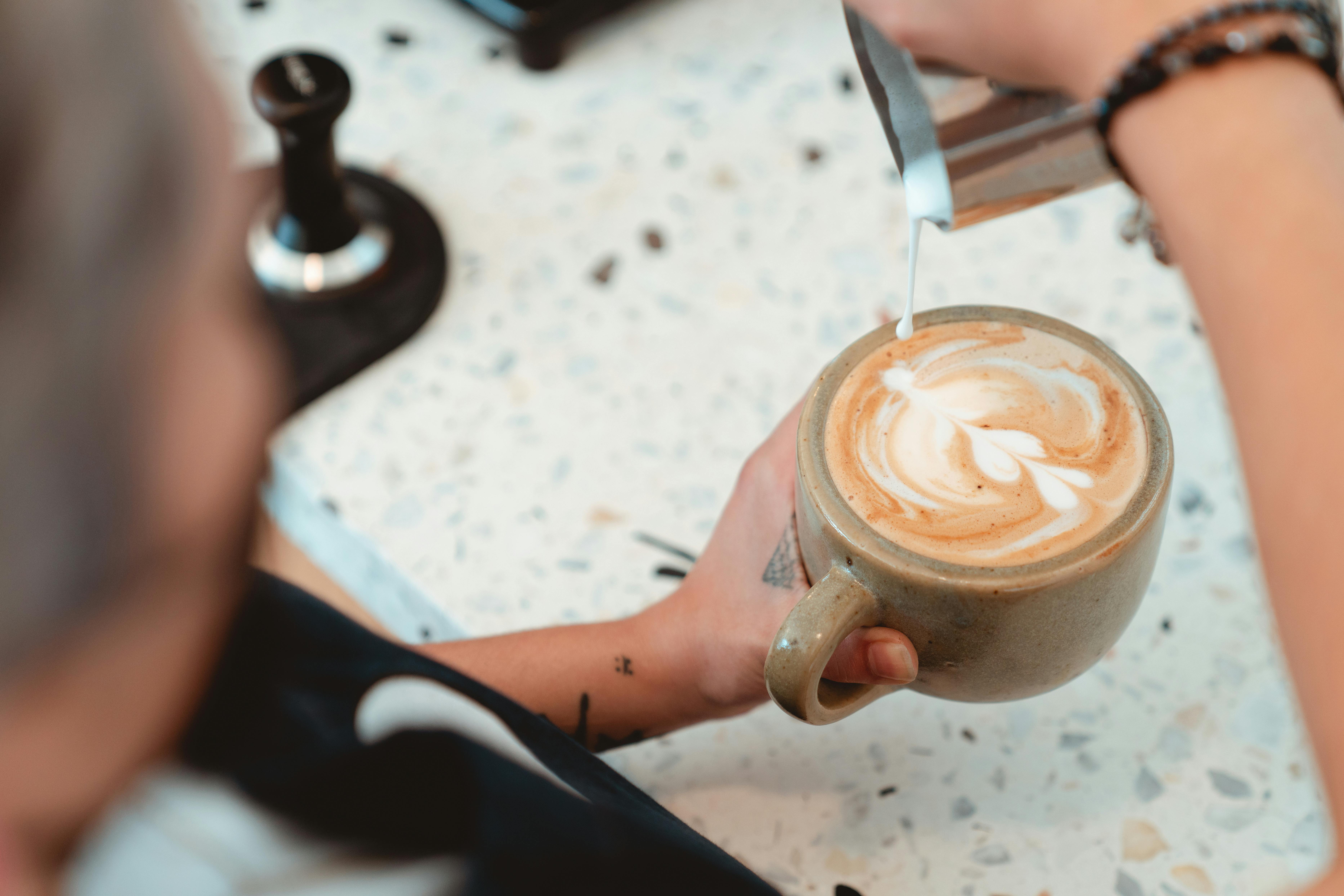 A professional barista pouring latte art into a ceramic cup with a French Bulldog illustration on the side.
